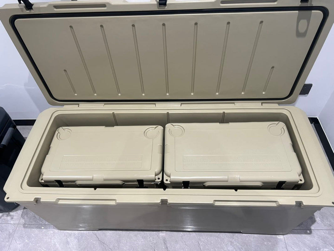 A large beige insulated cooler box with its lid open, showing two smaller matching cooler boxes nested inside on a gray tiled floor.